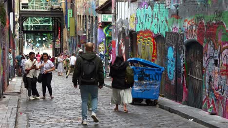 People-walking-through-popular-Hosier-Lane,-a-cobblestone-laneway-with-a-vibrant-array-of-art-murals-and-graffiti-on-the-walls,-a-creative-cultural-street-scene-in-Melbourne-city,-Victoria