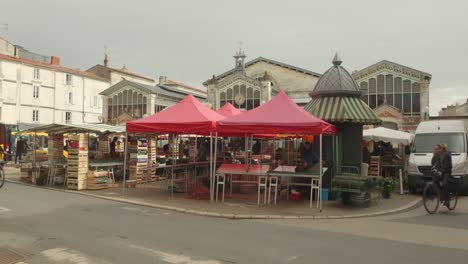 Pan-shot-of-a-historic-landmark-and-fresh-outdoor-food-market-called-Les-Halles-in-La-Rochelle,-France-on-a-cloudy-day