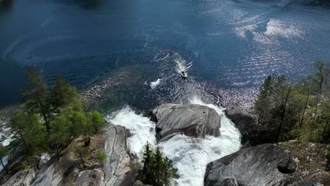 Tourists-in-a-RIB-boat-enter-Tysseknappen-Triple-Waterfall-at-Bolstadfjorden-Norway,-Aerial-above-waterfall