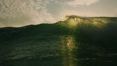 Backlit-ocean-wave-crashes-into-glassy-barrel-with-foam-and-underwater-vortex