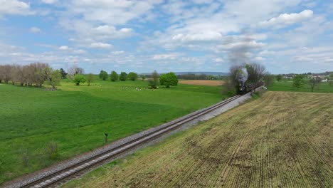 An-Aerial-View-of-an-Antique-Steam-Passenger-Train-Approaching,-Traveling-Thru-Rural-Countryside-on-a-sunny-Day