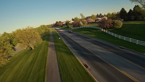 Aerial-tracking-shot-of-black-car-on-road-during-golden-sunrise