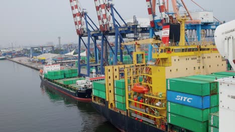 Vista-Del-Buque-De-Carga-Con-Contenedores-Apilados-Listos-Para-Entregar-Con-Grúas-Portuarias-En-El-Muelle.