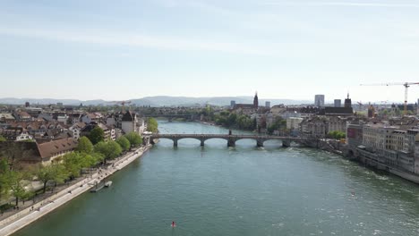 Aerial-of-a-bridge-spanning-the-Rhine-River-in-Basel,-Switzerland,-highlighting-the-seamless-integration-of-cityscape-and-natural-splendor,-embodying-connectivity-and-serene-landscapes