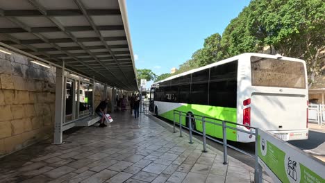 Walking-along-the-public-bus-station-in-Malta,-with-people-boarding-and-buses-waiting-at-stops