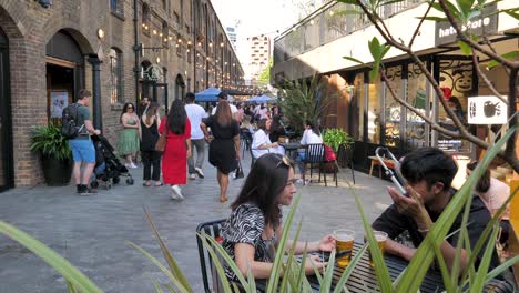 People-walking-along-storefronts-in-Coal-Drops-Yard-with-various-shops-and-restaurants,-King's-Cross,-London,-UK,-July-2023