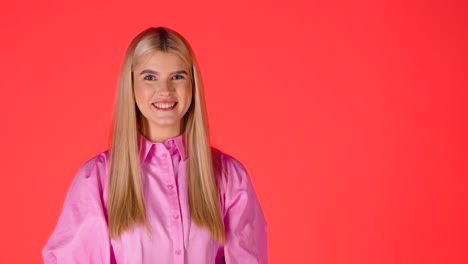 Mujer-Bonita-Rubia-Lanzando-Un-Globo-De-Corazón-Púrpura-En-El-Aire-Y-Luego-Sonriendo-A-La-Cámara,-Foto-De-Estudio-De-Fondo-Rojo