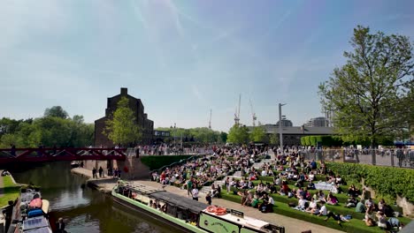 Crowd-enjoying-sunny-day-at-Kings-Cross-canalside-green-steps,-London