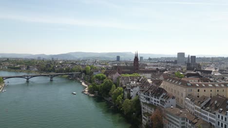 Aerial-view-of-Basel,-Switzerland,-spanning-over-the-river-and-up-to-The-Elisabethenkirche,-a-prime-example-of-Swiss-Gothic-architecture,-blending-historical-grandeur-with-modern-urbanity