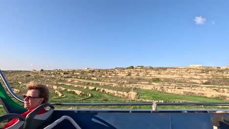 View-from-the-top-deck-of-a-tourist-bus-moving-along-the-island-of-Gozo,-Malta,-capturing-the-scenic-landscapes-and-cultural-charm