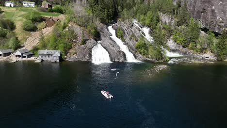 Tourists-on-RIB-boat-fjord-tour-outside-triple-waterfall-at-Tysseknappen-in-Norway,-aerial-view