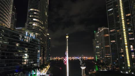 Bandera-Americana-Ondeando-Frente-Al-Horizonte-Urbano-En-El-Centro-De-Miami-Por-La-Noche