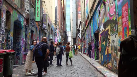 Tourists-walking-through-Hosier-Lane,-a-popular-cobblestone-laneway-with-a-vibrant-array-of-art-murals-and-graffiti-on-the-walls,-a-creative-cultural-street-scene-in-Melbourne-city,-Victoria