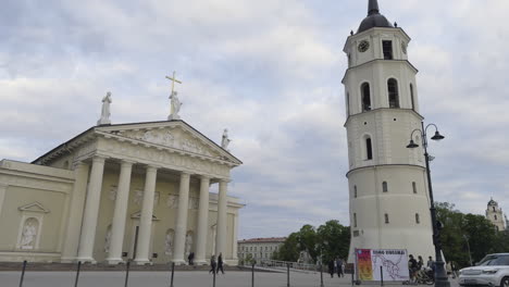 Catedral-De-Vilnius-En-Lituania,-Vista-Frontal-En-ángulo-Desde-El-Otro-Lado-De-La-Calle-Con-Santos-Y-Cruz-Encima-De-Los-Edificios-De-La-Iglesia