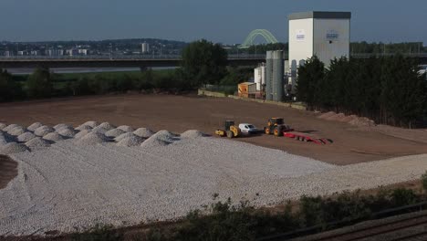 Aerial-view-approaching-construction-vehicles-working-on-sunlit-morning-laying-foundation-ground