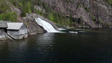 Barco-Turístico-Guiado-En-Noruega-Entrando-En-Una-Cascada-Para-Una-Experiencia-Divertida,-Cámara-Aérea-Lenta