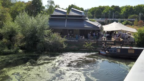 People-attending-a-garden-party-at-the-London-Wildlife-Trust-with-a-houseboat-in-the-canal-nearby,-King's-Cross,-London,-UK,-July-2023