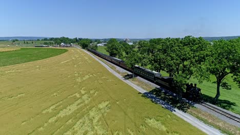 A-historic-steam-locomotive-powers-along-the-tracks,-past-golden-fields,-under-a-clear-blue-sky