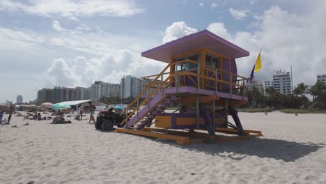 Colorida-Torre-De-Salvavidas-En-Miami-Beach-Con-Edificios-De-La-Ciudad-Al-Fondo-Bajo-Un-Cielo-Nublado