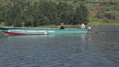 Locals-riding-long-wooden-motor-boat-in-Uganda,-side-view