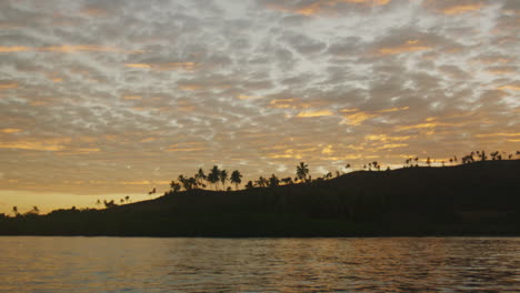 Epic-cloudscape-pattern-in-sky-catches-golden-red-light-at-sunrise-with-palm-tree-silhouette