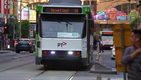 Pedestrians-crossing-the-crosswalk,-vehicle-traffic-and-tram-gliding-along-Elizabeth-streets-in-the-bustling-city-of-Melbourne,-a-vibrant-urban-street-scene-in-rush-hour