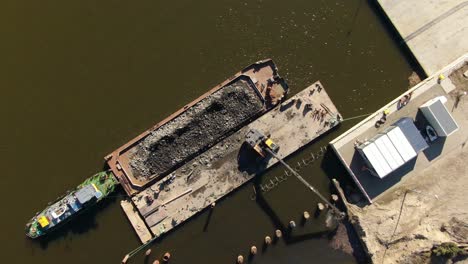 Top-down,-spinning-drone-shot-of-excavator-dumps-rubble-into-a-water