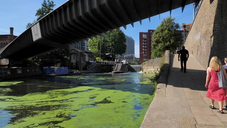 Vista-De-St-Pancras-Lock-Y-El-Puente-De-Somers-Town-Sobre-El-Canal-Regent-Con-Gente-Caminando-A-Lo-Largo-Del-Canal,-Londres,-Reino-Unido,-Julio-De-2023