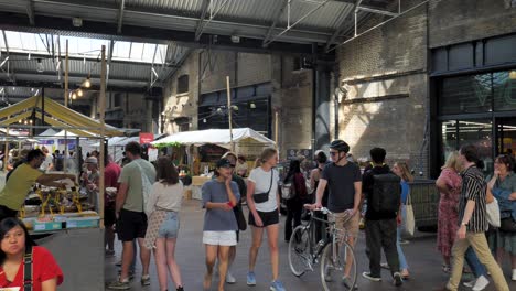 Gente-Explorando-Los-Puestos-De-Vendedores-En-El-Mercado-De-Dosel-Dentro-De-Un-Espacio-Cubierto-Con-Un-Ambiente-Animado,-King&#39;s-Cross,-Londres,-Reino-Unido,-Julio-De-2023