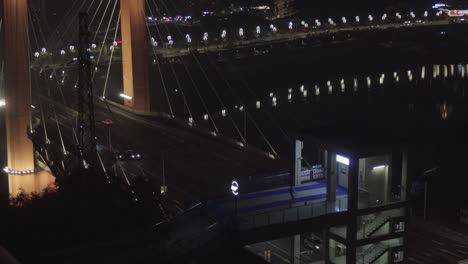 a-city-bridge-at-night-in-Chongqing,-with-sparse-vehicle-traffic-and-a-pedestrian-below-wearing-a-raincoat-and-dancing