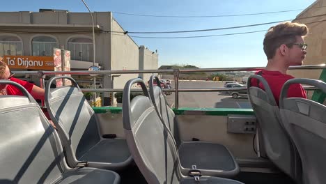 Travelers-and-visitors-ride-on-the-top-open-deck-of-a-touristic-bus-through-Gozo,-Malta,-capturing-the-scenic-landscapes-and-vibrant-atmosphere