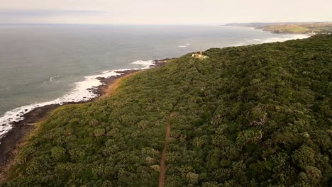 Lighthouse-perched-on-a-rugged-coast,-surrounded-by-lush-bushes-and-ocean---South-Africa