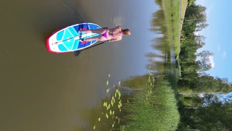 Volando-Por-Encima-De-Una-Joven-De-Pie-Remando-En-Una-Tabla-De-SUP-En-Un-Estanque-En-Verano