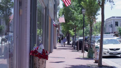 Sidewalk-in-downtown-Fredericksburg,-Virginia-with-gimbal-video-tilt-up-to-American-flags-flying-in-the-wind-in-slow-motion