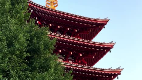 Red-pagoda-roof-detail-with-lush-green-tree-in-foreground-against-blue-sky