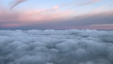 POV-Aufnahme-Einer-Himmlischen-Wolkenlandschaft-Aus-Einer-Flugzeugkabine,-Die-Bei-Sonnenuntergang-über-Einer-Schicht-Flauschiger-Wolken-Und-Einem-Pastellfarbenen-Himmel-Fliegt