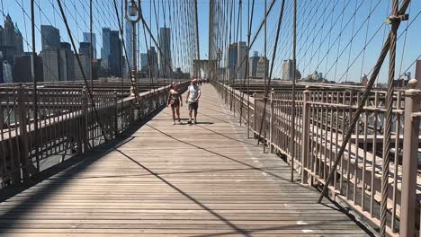 A-couple-walking-towards-the-camera-in-slow-motion-on-the-Brooklyn-Bridge-and-joking-with-each-other-in-New-York-City