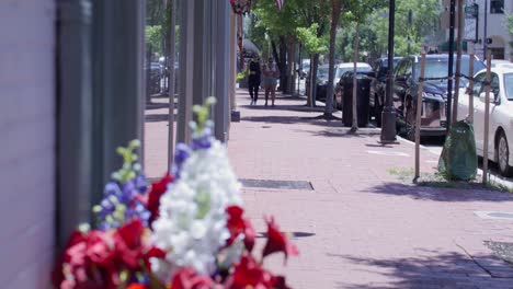 Flowers-in-downtown-Fredericksburg,-Virginia-with-gimbal-video-tilt-up-to-American-flags-flying-in-the-wind-in-slow-motion