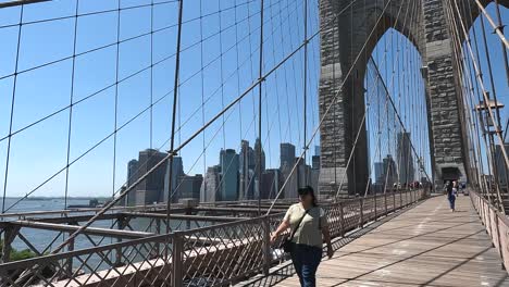 Eine-Mollige-Asiatische-Frau-Mittleren-Alters-Mit-Sonnenbrille-Und-Gelbem-Hemd-Läuft-Im-Frühsommer-2024-Auf-Der-Brooklyn-Bridge-In-New-York-City-Auf-Die-Kamera-Zu