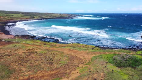 A-scenic-view-of-the-Hawaiian-coastline-with-crashing-waves,-rocky-shores,-and-lush-green-terrain-under-a-blue-sky