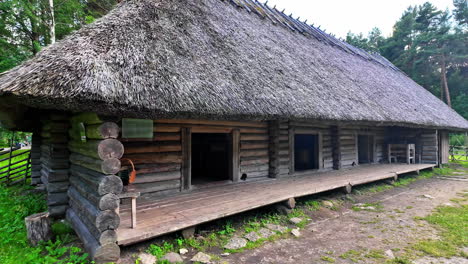 Close-up-shot-of-a-wooden-house-in-a-green-forest-of-Estonia,-slow-motion-left-to-right,-people-leaving-it-through-the-exit-on-the-right-side