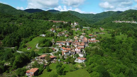 Beautiful-aerial-of-Italian-town-on-slopes-of-green-forested-hills,-Piedmont,-Italy