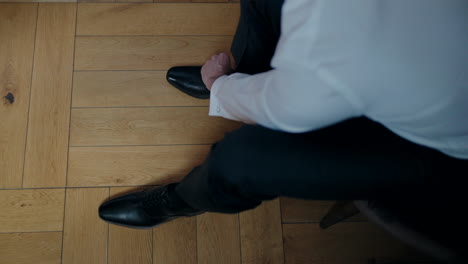 Man-in-a-white-shirt-and-dark-trousers-putting-on-black-shoes,-preparing-for-a-formal-event,-viewed-from-above