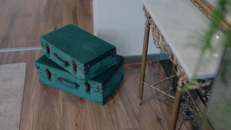 Two-vintage-green-suitcases-stacked-in-a-corner-of-a-room-with-wooden-floors-and-a-decorative-table