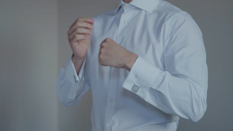 Man-in-a-white-shirt-adjusting-his-collar-and-fastening-his-cufflinks,-preparing-for-a-formal-event