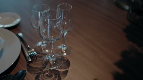 Close-up-of-empty-wine-glasses-arranged-on-a-wooden-table,-with-plates-and-cutlery-beside-them