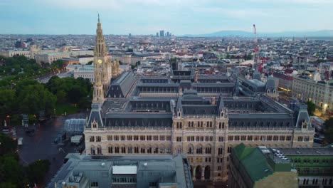 Drone-zooms-in-on-clock-tower-with-city-in-the-background,-soft-evening-light-and-sky