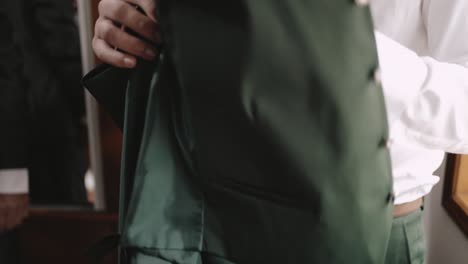 Man-in-a-white-shirt-and-green-tie-holding-a-green-jacket,-preparing-for-a-formal-event