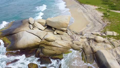 Drone-descending-view-of-water-waves-crashing-against-large-rock