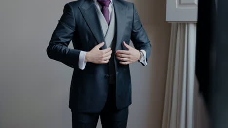 Man-in-a-dark-suit-with-a-grey-waistcoat-and-purple-tie,-adjusting-his-jacket,-preparing-for-a-formal-event